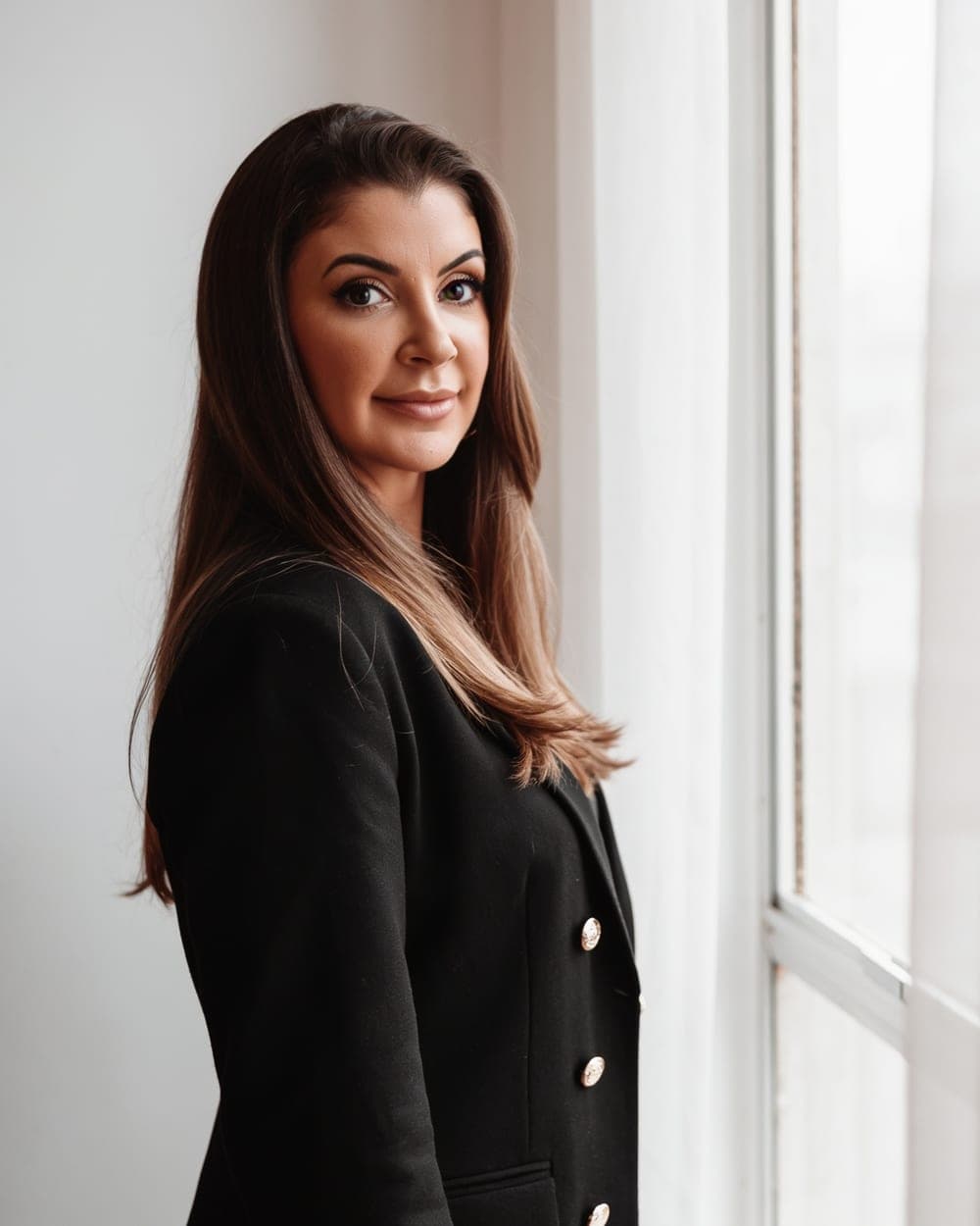 Mariana Rieping, advogada criminalista, de blazer preto junto à janela do escritório, OAB/PR 119.933 e OAB/SP 550.583